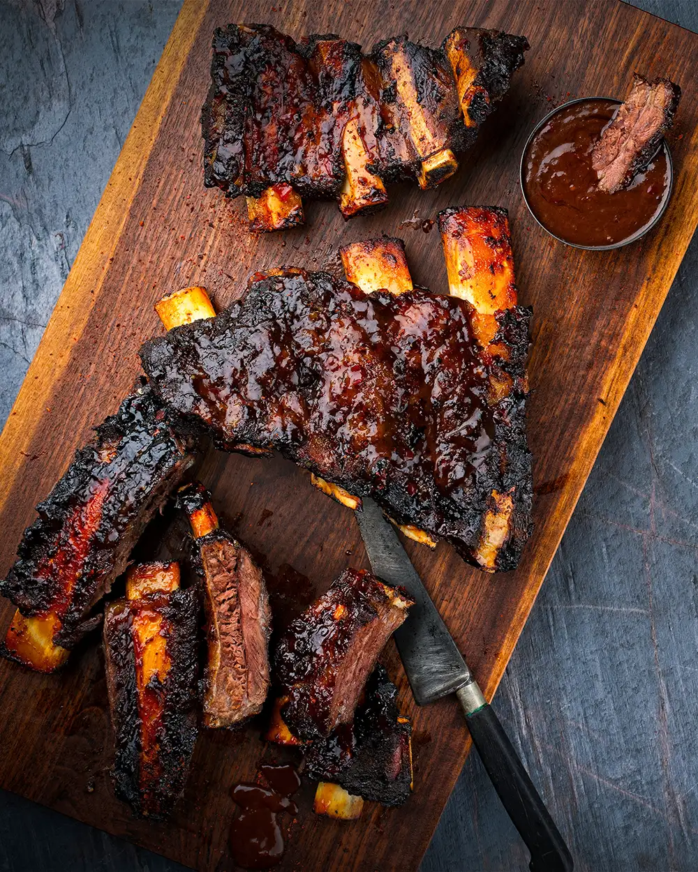 BBQ Barbecue Burnt Chuck Beef Ribs mariniert mit würzigem Rub und Grillsauce serviert als Draufsicht auf einem rustikalen Holzbrett